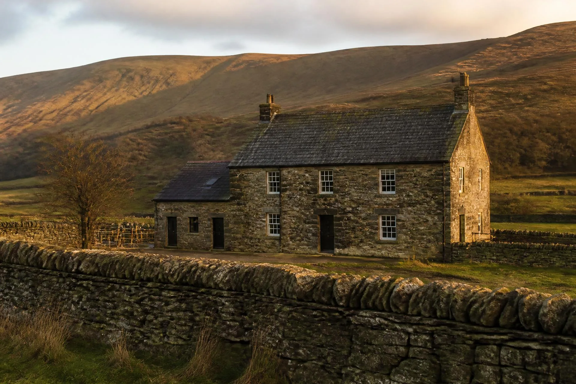 Stone farmhouse below open hillside in the Welsh borders at golden hour